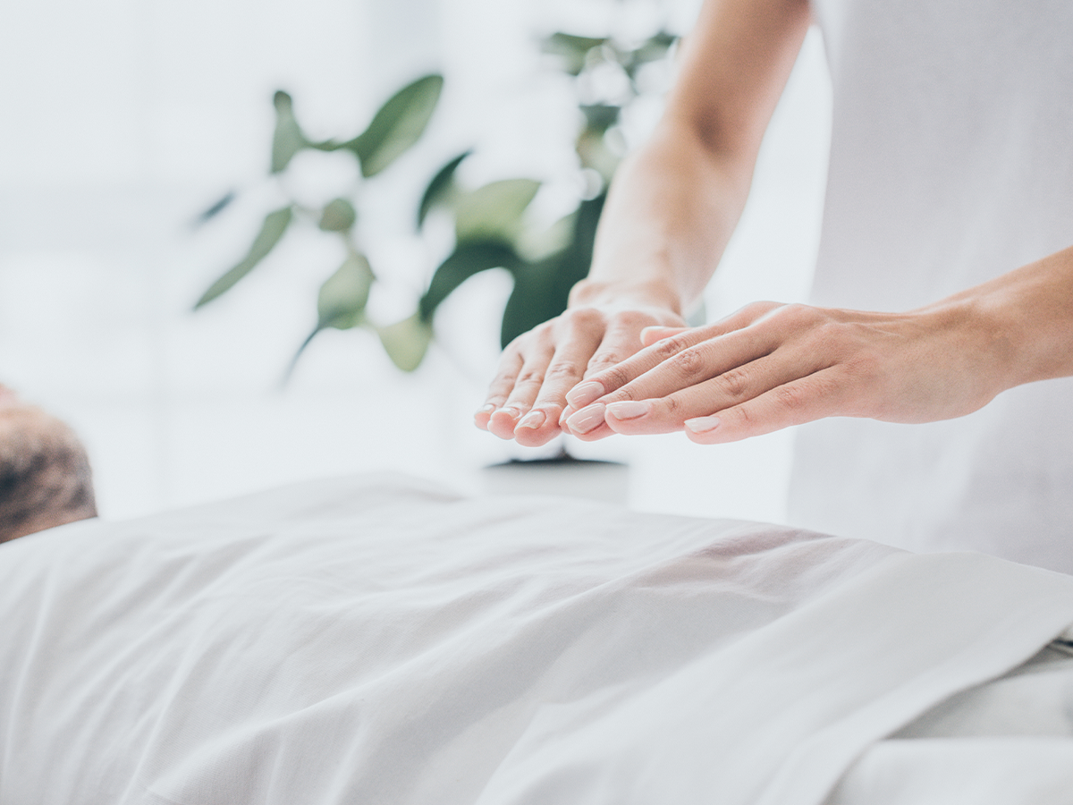 Photographie d'une séance de magnétisme : un patient est allongé, les mains du praticien se déplacent au dessus de son corps